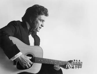 circa 1975:  Profile of American country singer Johnny Cash (1932 - 2003), wearing a tuxedo, playing an acoustic guitar, in a promotional still for the 11th annual Country Music Association Awards which Cash hosted at the Grand Ole Opry, Nashville, Tennessee.  (Photo by CBS Photo Archive/Getty Images)