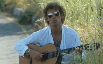 Italian singer-songwriter Franco Califano playing guitar on the roadside wearing a pair of sunglasses. 1981  (Photo by Rino Petrosino\Mondadori via Getty Images)