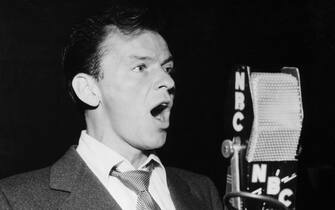 (Original Caption) Waist-up portrait of singer/actor Frank Sinatra singing into an NBC microphone. Undated photograph.