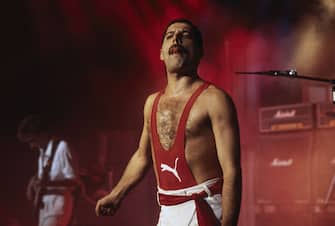 Singer Freddie Mercury sticks his tongue out while performing on stage with rock group Queen, 1984. He is wearing a red puma vest and white trousers. (Photo by Dave Hogan/Getty Images)