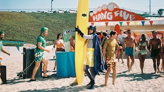 Adam West, US actor, wearing a pair of yellow and white long shorts over his costume, and standing on a beach with a yellow surfboard, with the Batman logo, in a publicity still issued for the 'Surf's Up! Joker's Under!' episode of the US television series, 'Batman', USA, 1967. The television series featuring DC Comics characters, starred West as 'Bruce Wayne' and his alter ego 'Batman'. (Photo by Silver Screen Collection/Getty Images)