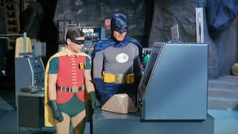 (Original Caption) Adam West at "Batman" and Bert Ward as "Robin" stand near the "Batmobile" during filming on an episode from the Batman television series.