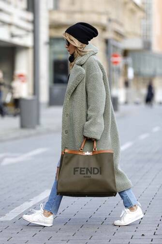 DUESSELDORF, GERMANY - NOVEMBER 13: Influencer Gitta Banko wearing a long sage green colored teddy coat by Stand Studio, light blue ripped denim jeans by Balenciaga, a black cashmere turtleneck pullover by Boscana, a black beanie, sunglasses by Bottega Veneta, a khaki colored canvas peekaboo shopper by Fendi, white and beige sneakers with butterflies by Sophia Webster during a street style shooting on November 13, 2020 in Duesseldorf, Germany. (Photo by Streetstyleshooters/Getty Images)