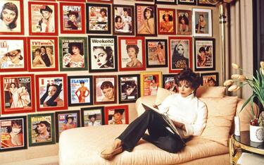 Actress Joan Collins wearing a white sweater and black pants, working on her novel in the office of her Beverly Hills, California home in November 1995. On the wall behind her are framed magazine covers of Joan from publications around the world. (Photo by Eddie Sanderson/Getty Images).