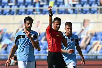 talian referee Marco Di Bello (C) shows a yellow card to Lazio's Italian midfielder Marco Parolo (L) during the Italian Serie A football match Lazio Rome vs Sassuolo played behind closed doors on July 11, 2020 at the Olympic stadium in Rome, as the country eases its lockdown aimed at curbing the spread of the COVID-19 infection, caused by the novel coronavirus. (Photo by Vincenzo PINTO / AFP) (Photo by VINCENZO PINTO/AFP via Getty Images)