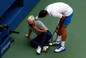 epa08651640 Novak Djokovic of Serbia (R) tries to help a linesperson after hitting her with a ball in the throat during his match against Pablo Carreno Busta of Spain on the seventh day of the US Open Tennis Championships at the USTA National Tennis Center in Flushing Meadows, New York, USA, 06 September 2020. Djokovic was defaulted from tournament. Due to the coronavirus pandemic, the US Open is being played without fans and runs from 31 August through 13 September.  EPA/JASON SZENES