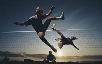 736396677 Competitors acrobatically jump to kick the ball over the net during a Sepak Takraw (Kick-Volleyball) match on the beach at sunset on1 June 1991 at Malibu, California, United States. Visions of Sport. (Photo by Mike Powell/Allsport/Getty Images)