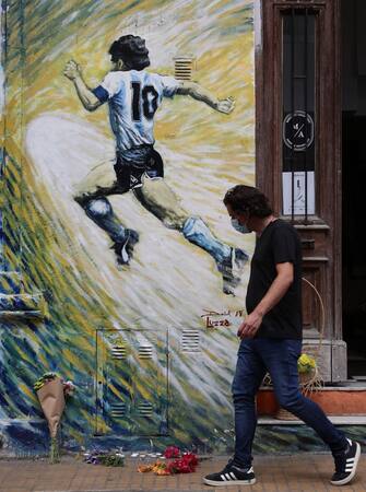 A man walks past flowers left next to a mural depicting Argentine football star Diego Maradona, in San Telmo neighborhood, Buenos Aires on November 25, 2020, on the day of his death. (Photo by ALEJANDRO PAGNI / AFP) (Photo by ALEJANDRO PAGNI/AFP via Getty Images)