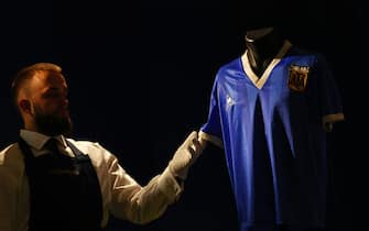 A Sotheby's technician adjusts a football shirt worn by Argentina's Diego Maradona during the 1986 World Cup quarter-final match against England, during a photocall at Sotheby's auction house in London on April 20, 2022, ahead of its sale. - The jersey worn by Diego Maradona when he scored twice against England in the 1986 World Cup, including the infamous "hand of God" goal, is to be auctioned off this month, Sotheby's announced Wednesday. The blue number 10 shirt has been owned since the end of the controversial World Cup encounter by opposing midfielder Steve Hodge, who swapped his jersey with Maradona after England lost 2-1. (Photo by ADRIAN DENNIS / AFP) (Photo by ADRIAN DENNIS/AFP via Getty Images)