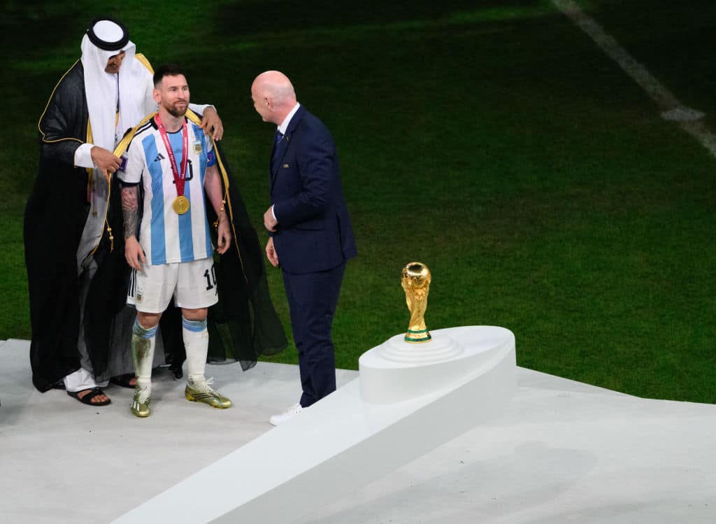 18 December 2022, Qatar, Lusail: Soccer, World Cup, Argentina - France, final round, final, Lusail Stadium, the Emir of Qatar, Sheikh Tamim bin Hamad Al Thani (l), puts on Argentina's Lionel Messi a bisht, a traditional Arab garment, in front of Fifa President Gianni Infantino before handing over the World Cup trophy. Photo: Robert Michael/dpa - IMPORTANT NOTE: In accordance with the requirements of the DFL Deutsche FuÃ ball Liga and the DFB Deutscher FuÃ ball-Bund, it is prohibited to use or have used photographs taken in the stadium and/or of the match in the form of sequence pictures and/or video-like photo series. (Photo by Robert Michael/picture alliance via Getty Images)