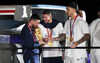 epa10374435 Lionel Messi of the Argentina national soccer team holds the trophy of Qatar 2022 World Cup next to Rodrigo De Paul (C) and Leandro Paredes upon ther arrival to International Airport of Ezeiza, some 22km of Buenos Aires, Argentina, 20 December 2022.  EPA/RAUL MARTINEZ