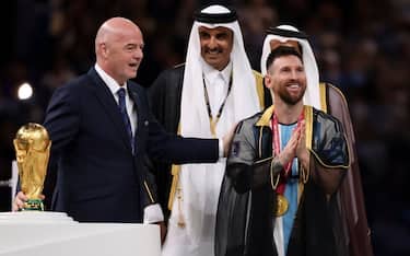 LUSAIL CITY, QATAR - DECEMBER 18: FIFA President Gianni Infantino, Emir of Qatar Sheikh Tamim bin Hamad Al Thani and Lionel Messi of Argentina wearing a traditional black robe called bisht during the trophy ceremony following the FIFA World Cup Qatar 2022 Final match between Argentina and France at Lusail Stadium on December 18, 2022 in Lusail City, Qatar. (Photo by Jean Catuffe/Getty Images)