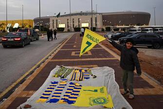 epa10387401 A child holds a flag with Ronaldo's name while selling souvenirs outside Mrsool Park stadium where Portuguese soccer player Cristiano Ronaldo will be presented, in Riyadh, Saudi Arabia, 03 January 2023. Cristiano Ronaldo will be presented at Mrsool Park stadium on 03 January after he signed a contract for Al-Nassr FC untill 2025.  EPA/STR