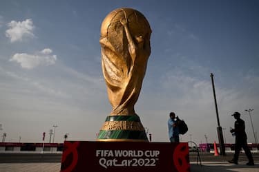 TOPSHOT - Men walk past a FIFA World Cup trophy replica outside the Ahmed bin Ali Stadium in Al-Rayyan on November 12, 2022, ahead of the Qatar 2022 FIFA World Cup football tournament. (Photo by Kirill KUDRYAVTSEV / AFP) (Photo by KIRILL KUDRYAVTSEV/AFP via Getty Images)