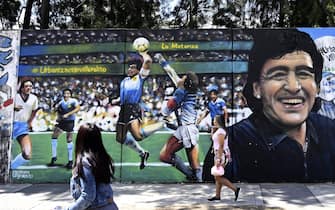 Women walk past a mural by street artist "Uasen" depicting Argentine former football star Diego Maradona -current coach of Gimnasia y Esgrima La Plata football team- scoring the first goal in the FIFA World Cup Mexico 86 match against England, in Villa Palito, San Justo, La Matanza, Buenos Aires province, Argentina, on October 30, 2020 on Maradona's 60th birthday. (Photo by JUAN MABROMATA / AFP) (Photo by JUAN MABROMATA/AFP via Getty Images)