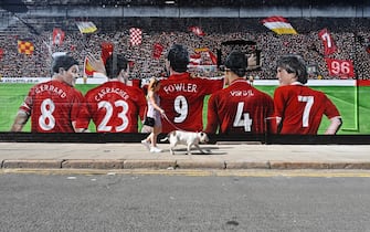 A woman walks her dog past a mural on the side of a hotel depicting Liverpool football club former players (L-R) Steven Gerrard, Jamie Carragher, Robbie Fowler, current defender Virgil van Dijk and former player and manager Kenny Dalglish in Anfield, Liverpool, northwest England, on September 12, 2020. (Photo by Paul ELLIS / AFP) (Photo by PAUL ELLIS/AFP via Getty Images)