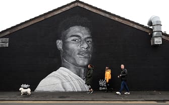 Pedestrians walk past a mural by grafitti artist Akse P19 of Manchester United football player Marcus Rashford on teh side of a building in Withington, Manchester, northwest England on November 8, 2020. - The UK government on November 8 relented anew to a vocal campaign by Manchester United star Marcus Rashford, promising to give free meals to poorer children over the coronavirus-afflicted Christmas holidays and beyond. (Photo by Paul ELLIS / AFP) / RESTRICTED TO EDITORIAL USE - MANDATORY MENTION OF THE ARTIST UPON PUBLICATION - TO ILLUSTRATE THE EVENT AS SPECIFIED IN THE CAPTION (Photo by PAUL ELLIS/AFP via Getty Images)