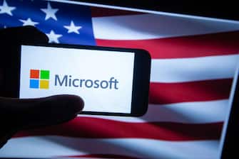 The logo of Microsoft is seen on a screen in front of an American flag. It is listed in the Dow Jones as it is one of the major US companies on the stock market. (Photo by Alexander Pohl/NurPhoto via Getty Images)