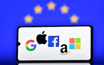 Un telefono con loghi delle Big Tech sullo sfondo la bandiera europea