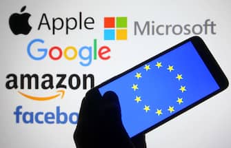 Un telefono con bandiera europea sullo sfondo i loghi delle Big Tech