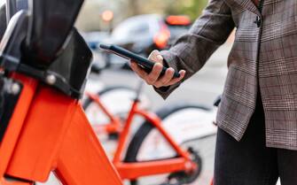 1355328099 Woman using QR code on smart phone to rent a bike in city - Commuting and urban lifestyle