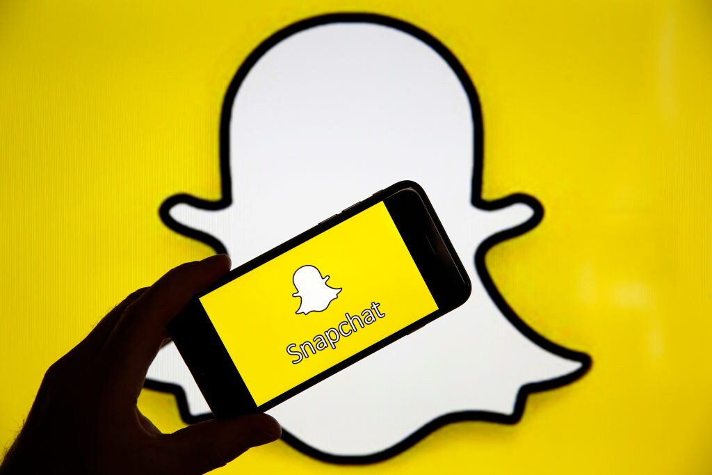 1140608006 PARIS, FRANCE - APRIL 05: In this photo iIllustration, the Snapchat social media logo is displayed on the screen of an iPhone in front of a computer screen showing a Snapchat logo on April 05, 2019 in Paris, France. During its 'Partner Summit 2019' in Santa Monica, Snapchat has announced several new features to come. Most notable is the ability to send stories to the Tinder dating app. Snapchat is a free photo and video sharing application which has 13 million daily users worldwide. (Photo by Chesnot/Getty Images)