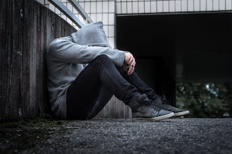 Depression, social isolation, loneliness, mental health and discrimination concept. Sad, lonely, depressed and unhappy man. Hooded person sitting.
